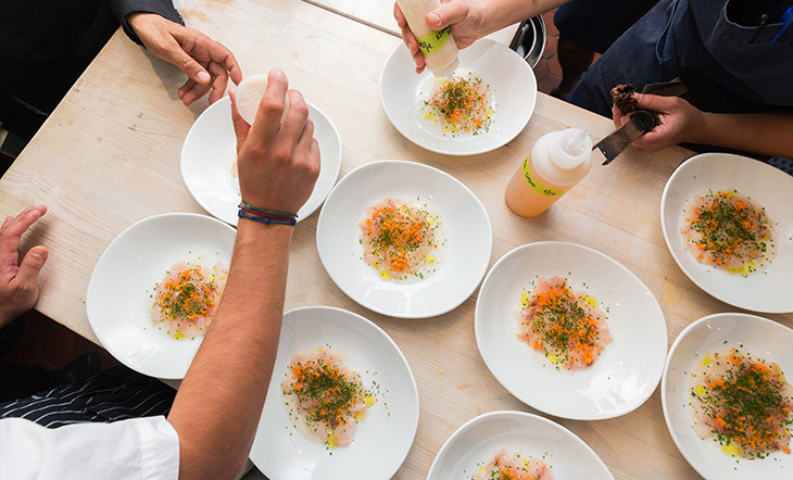 Image of dishes being prepared on a wooden background with chefs plating